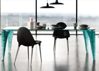 Mesa Atlas: una escultura de vidrio convertida en mueble Mesa Atlas de vidrio con patas esculpidas, rodeada de sillas negras en un comedor moderno.